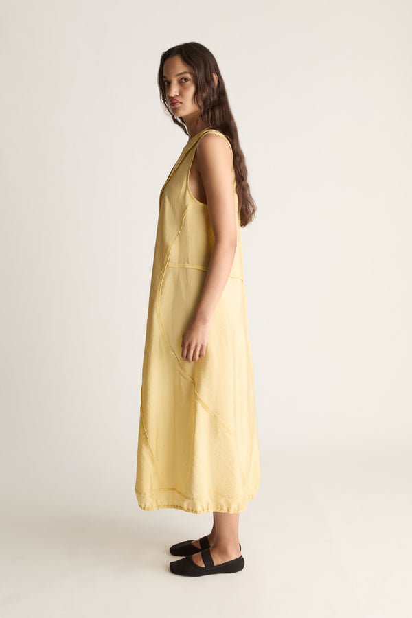 Side view of a woman looking over her shoulder in a yellow sleeveless midi dress and black ballet flats