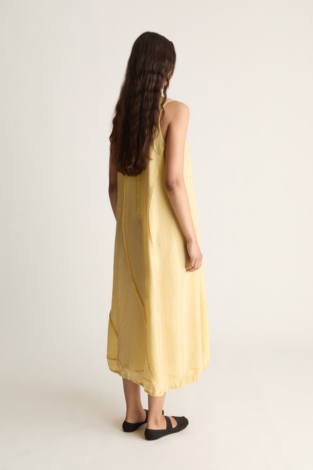 Back view of a woman with long wavy hair in a loose yellow sleeveless midi dress