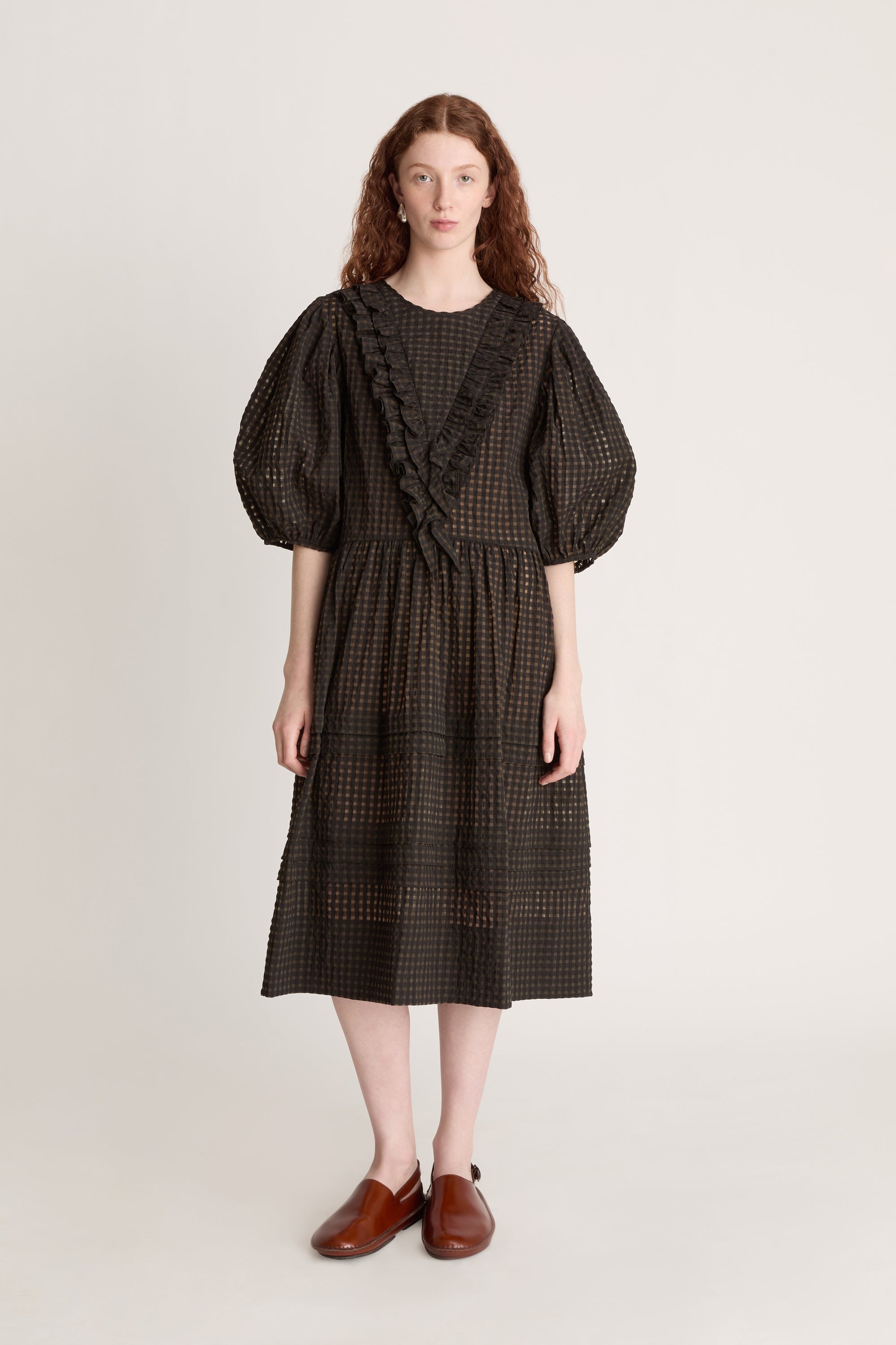 Woman wearing a dark checkered dress  with puffy sleeves with ruffled details on a white background