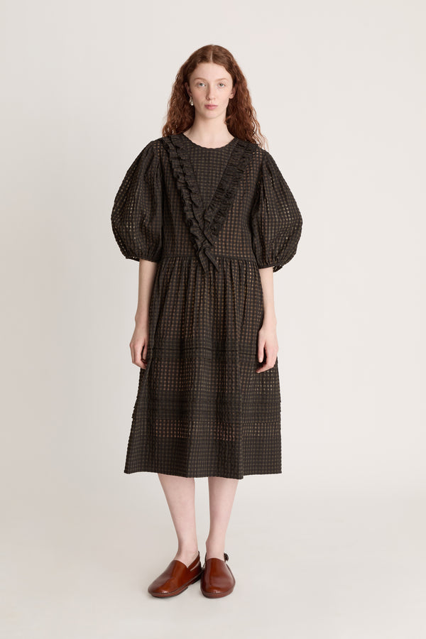 Woman wearing a dark checkered dress  with puffy sleeves with ruffled details on a white background
