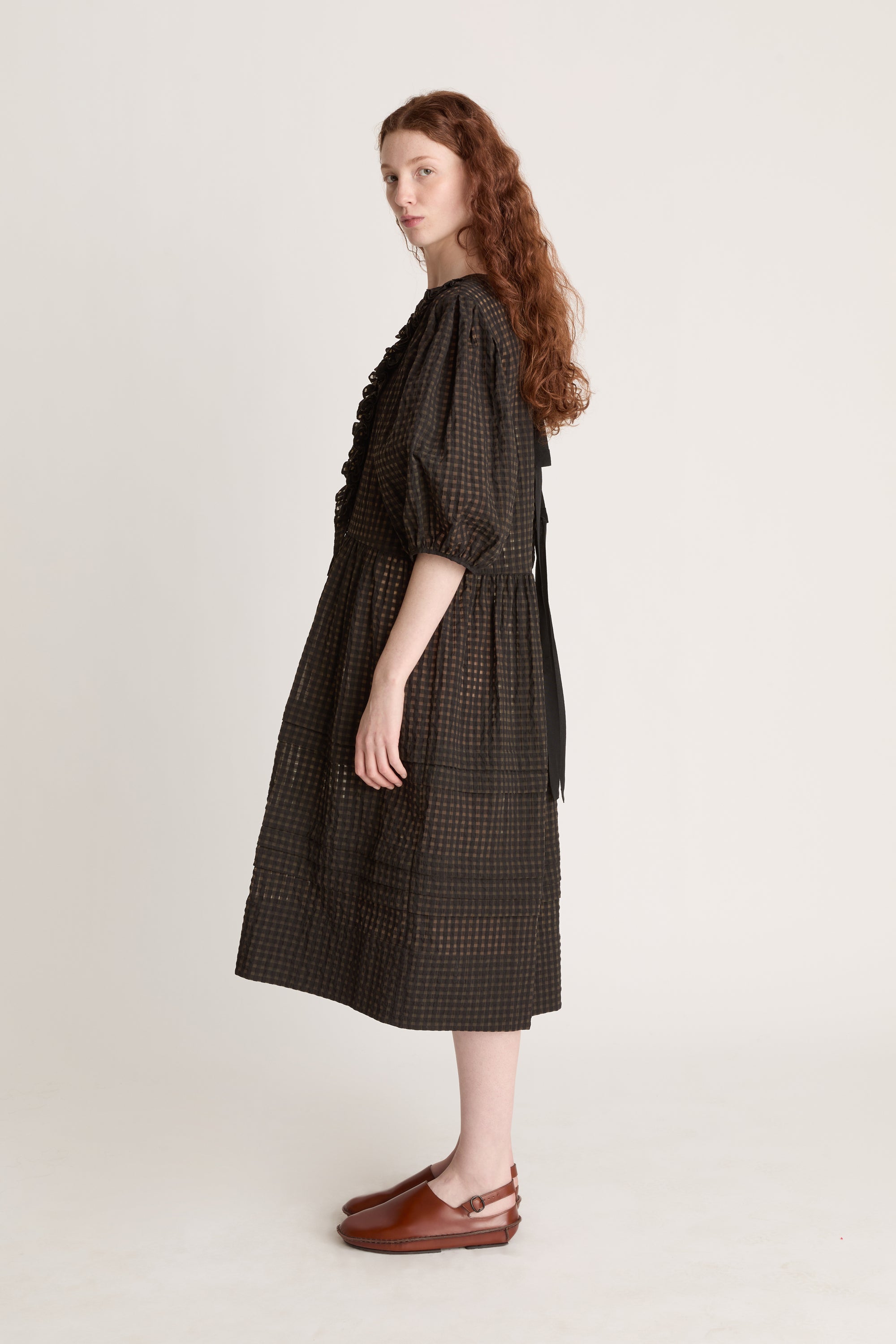 Woman wearing a dark checkered dress  with puffy sleeves with ruffled details on a white background