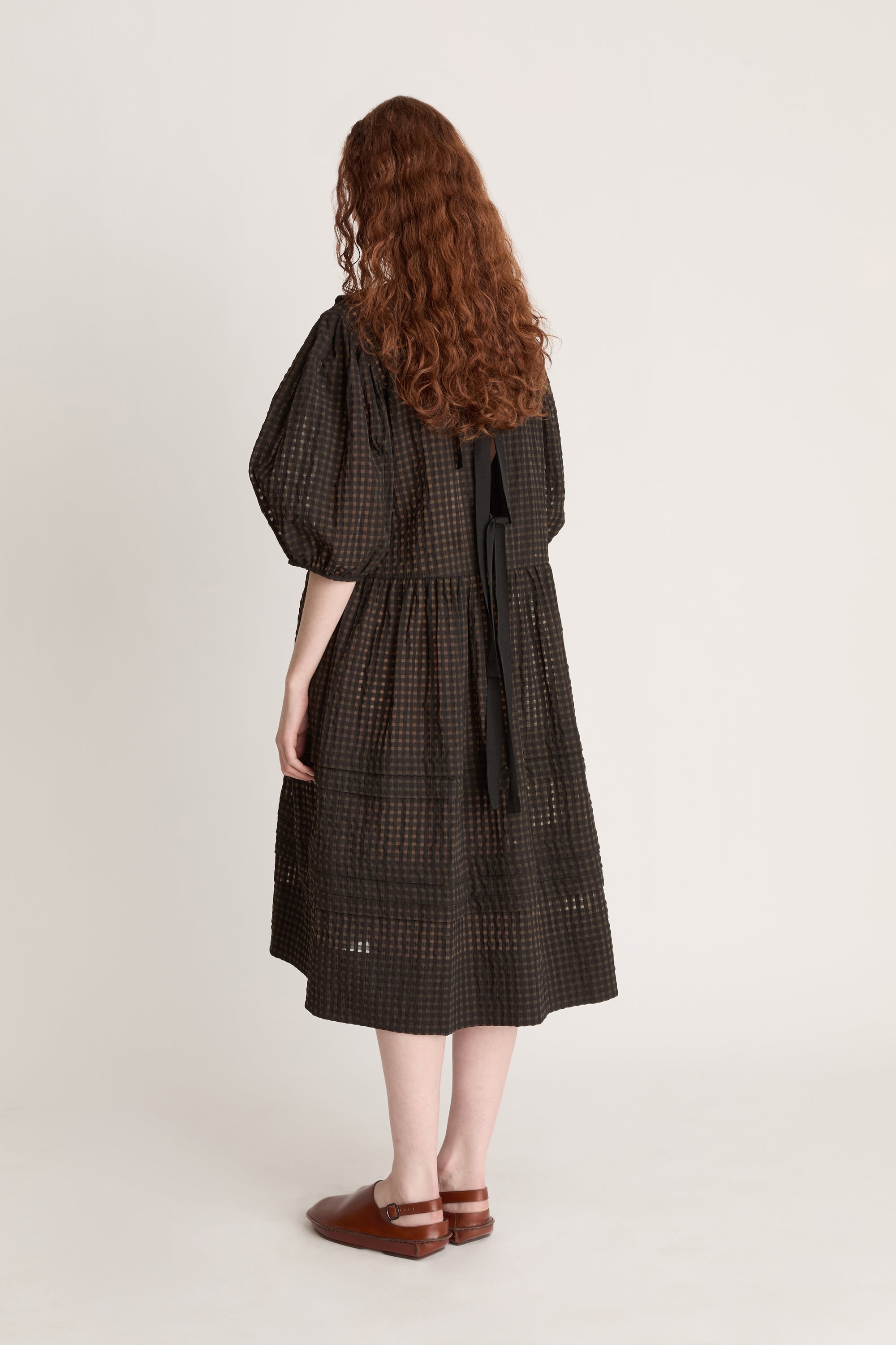Woman wearing a dark checkered dress  with puffy sleeves with ruffled details on a white background