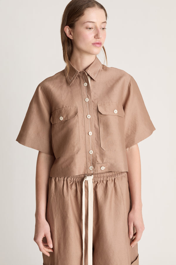 Woman wearing a brown button up short sleeve shirt and brown pants on a white background 