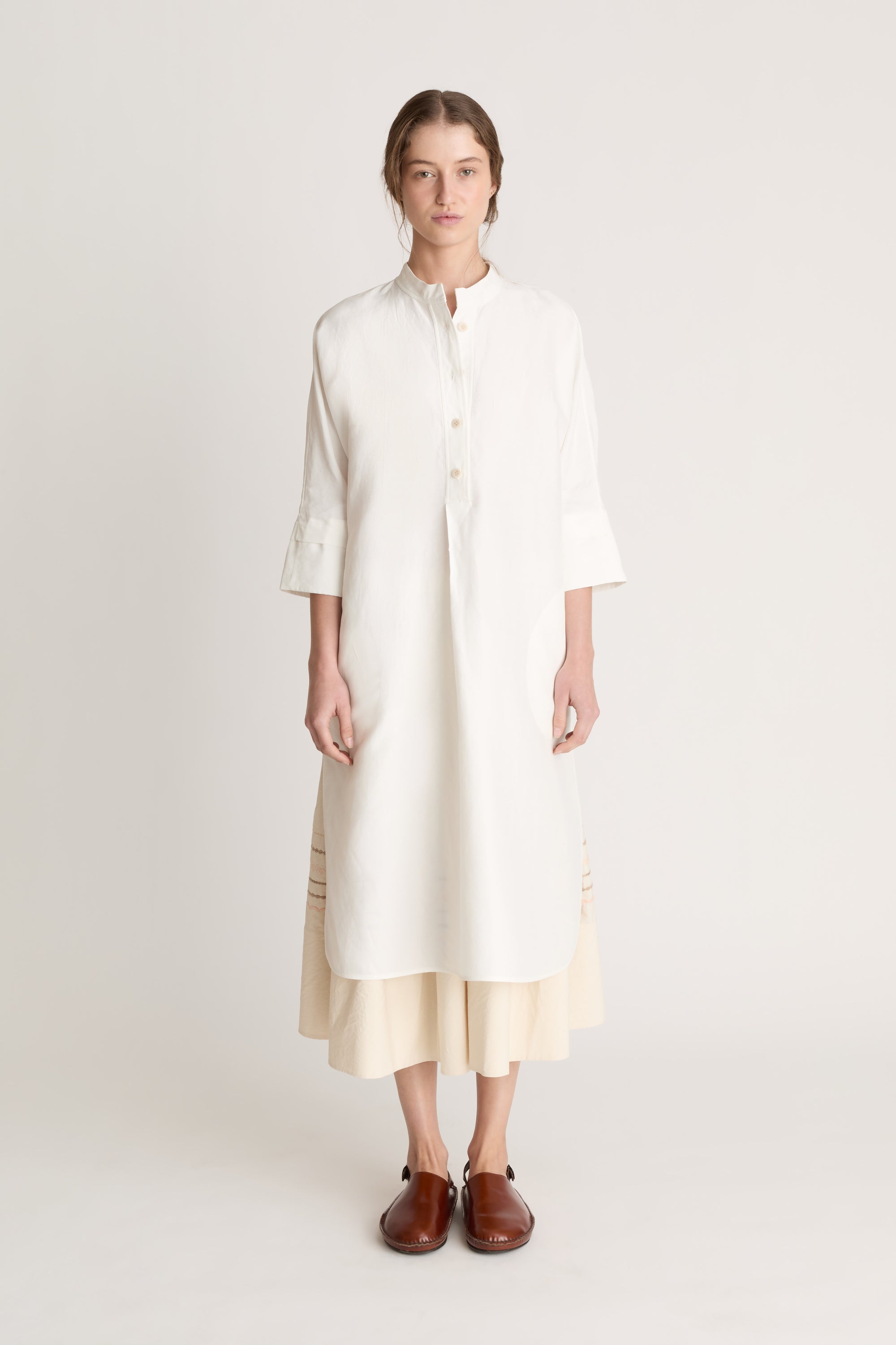 Woman wearing a white tunic with a beige skirt on a white background
