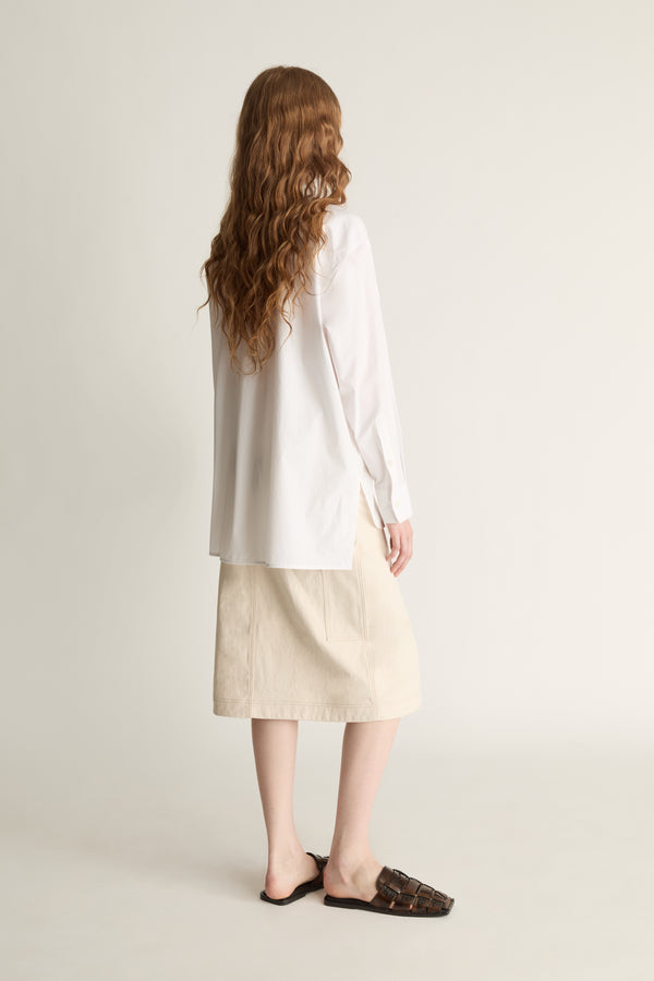 Person wearing a white shirt and beige skirt on a plain background