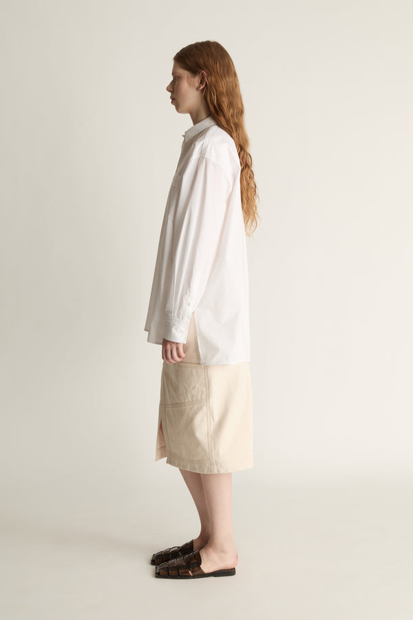 Person wearing a white shirt and beige skirt on a plain background