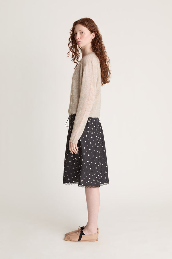 Woman wearing a beige knit cami top and cardigan with a black printed skirt on a white background