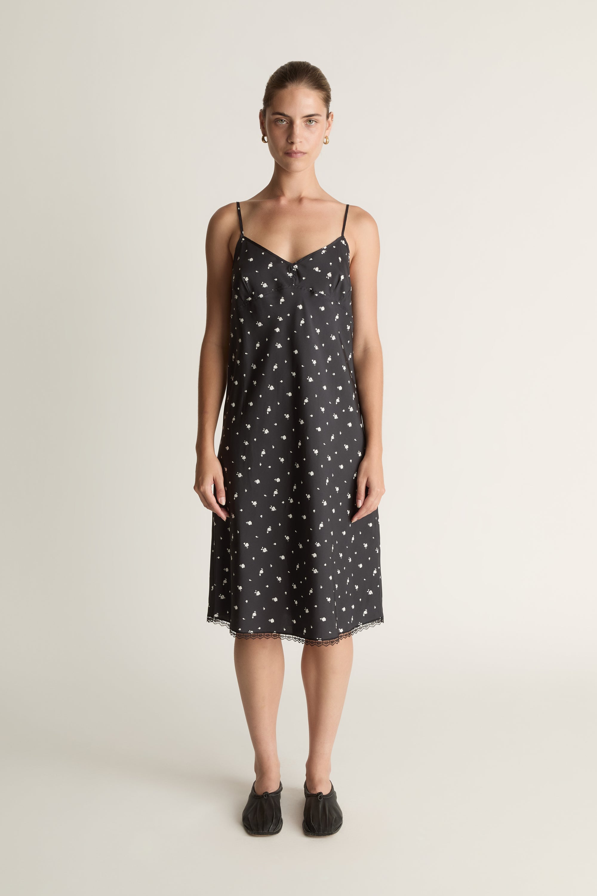 Woman wearing a black slip dress with white floral print on a plain background