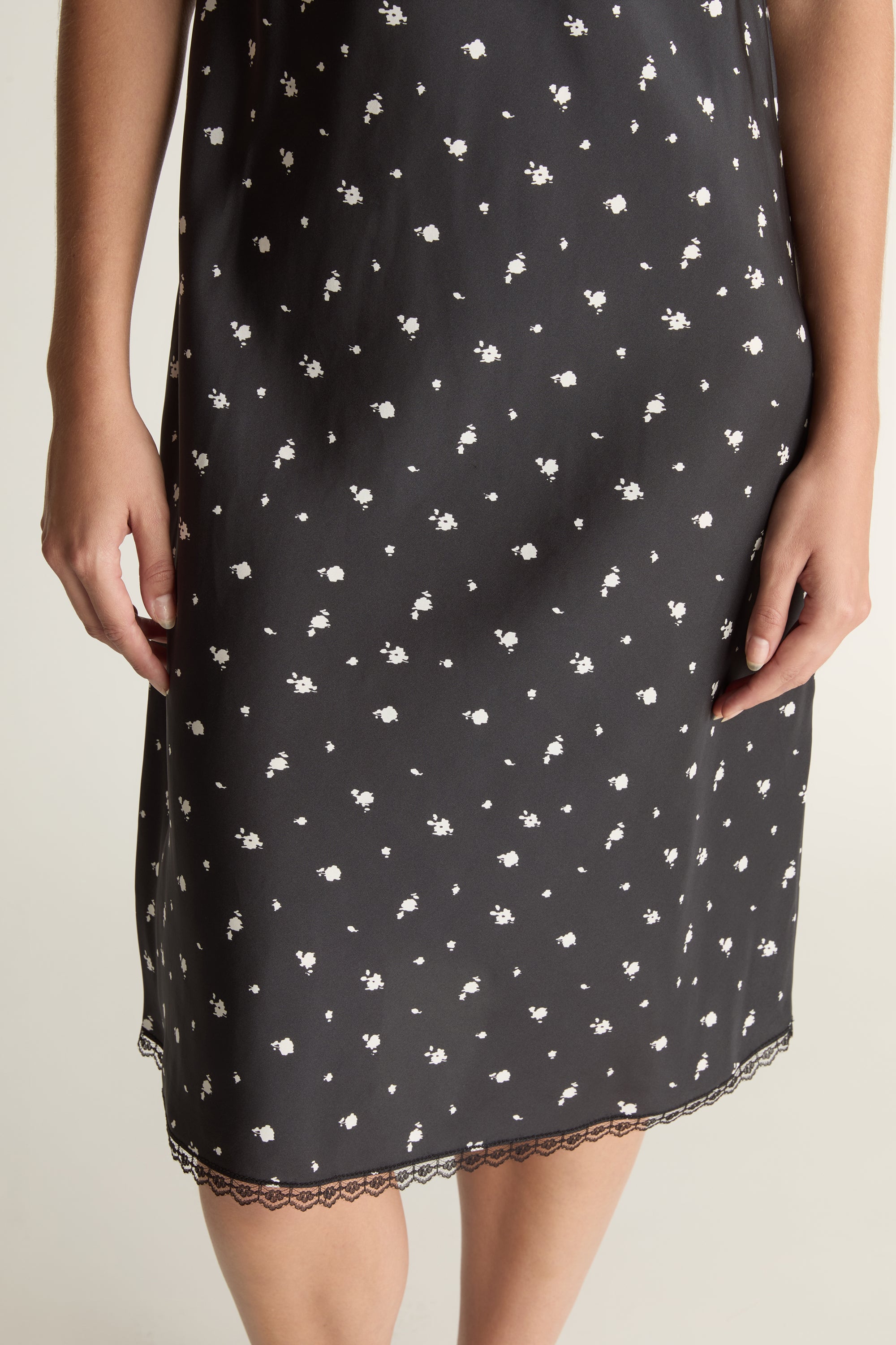 Woman wearing a black slip dress with white floral print on a plain background
