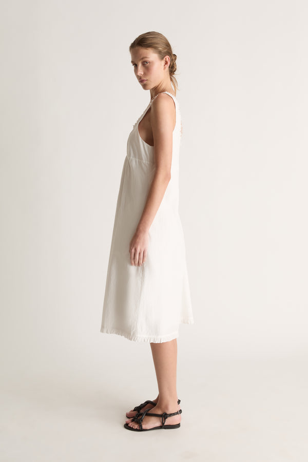 Side profile of a woman looking over her shoulder in a white sleeveless midi dress with ruffled edge