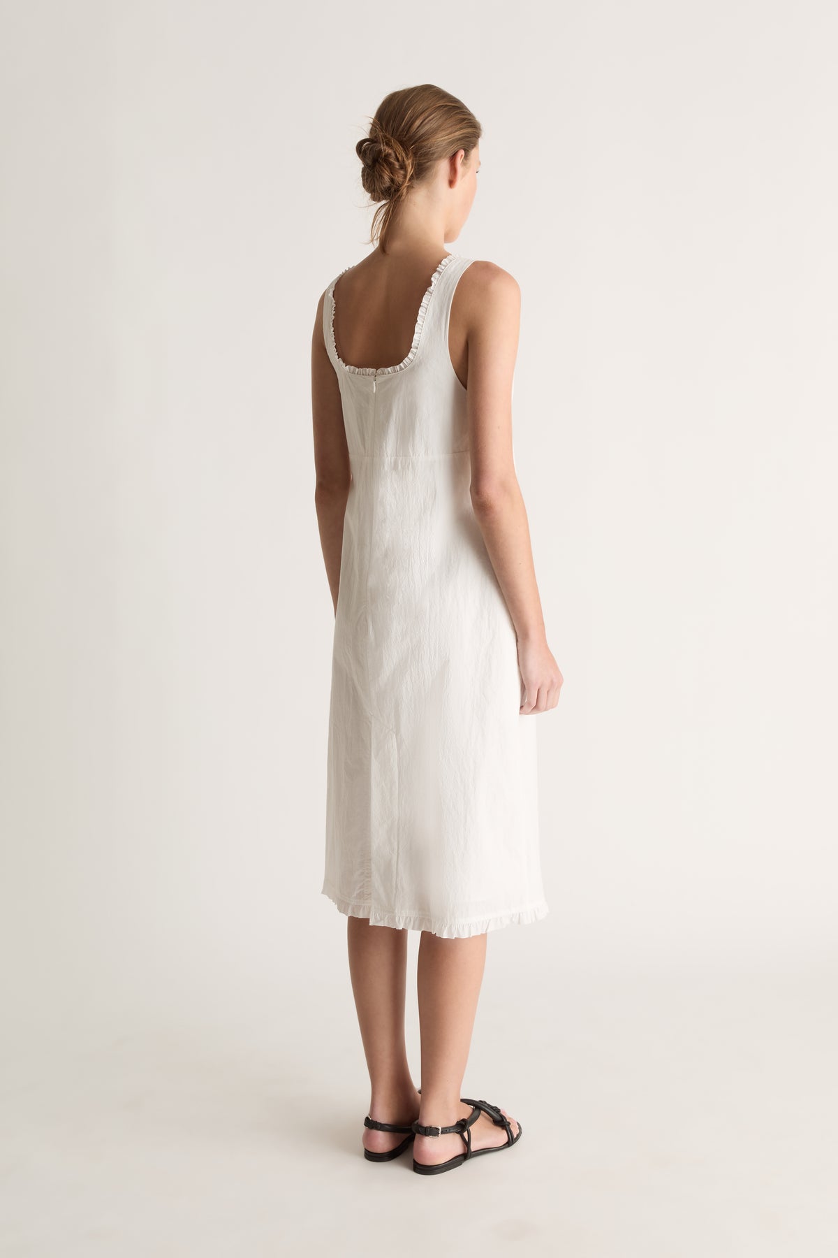 Back view of a woman with a low bun in a white dress with a ruffle-trimmed scoop back