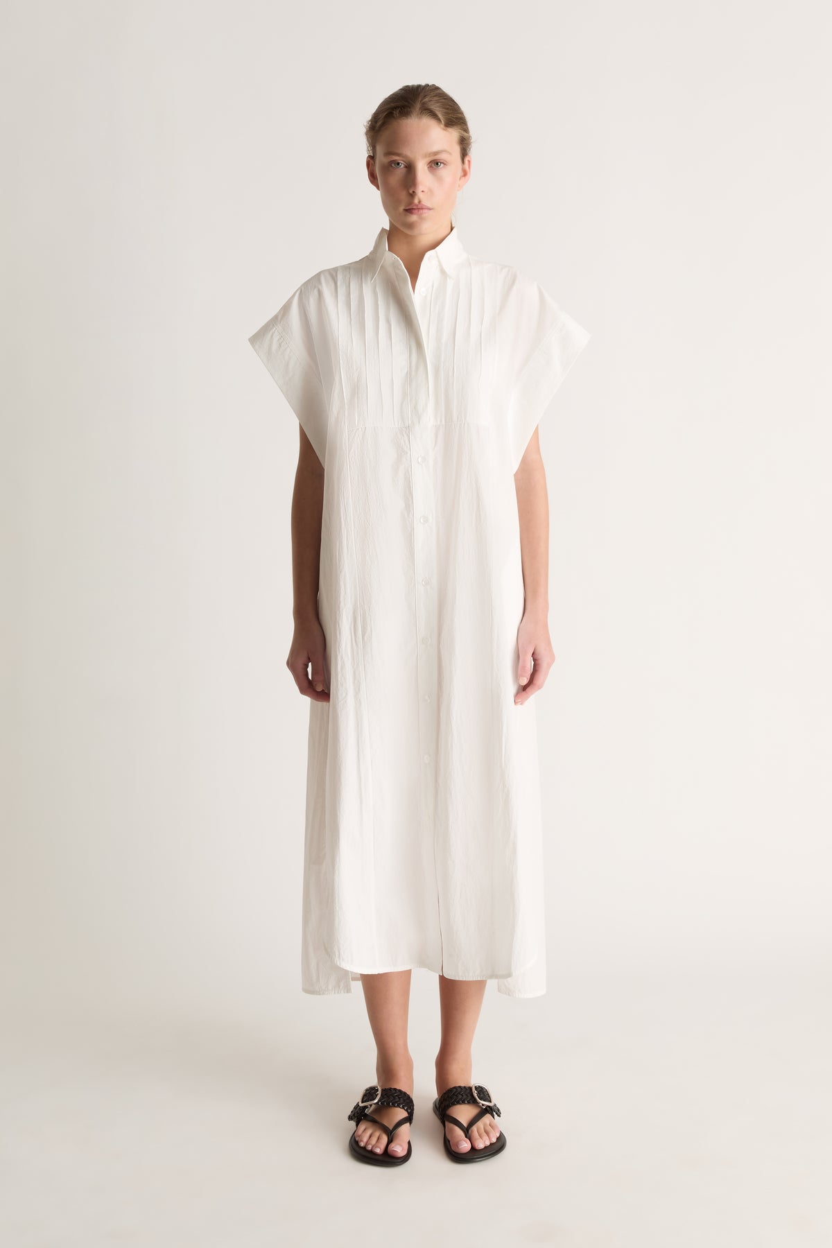 Front view of a white midi shirt dress with wide cap sleeves, a pin-tucked bib and button front.