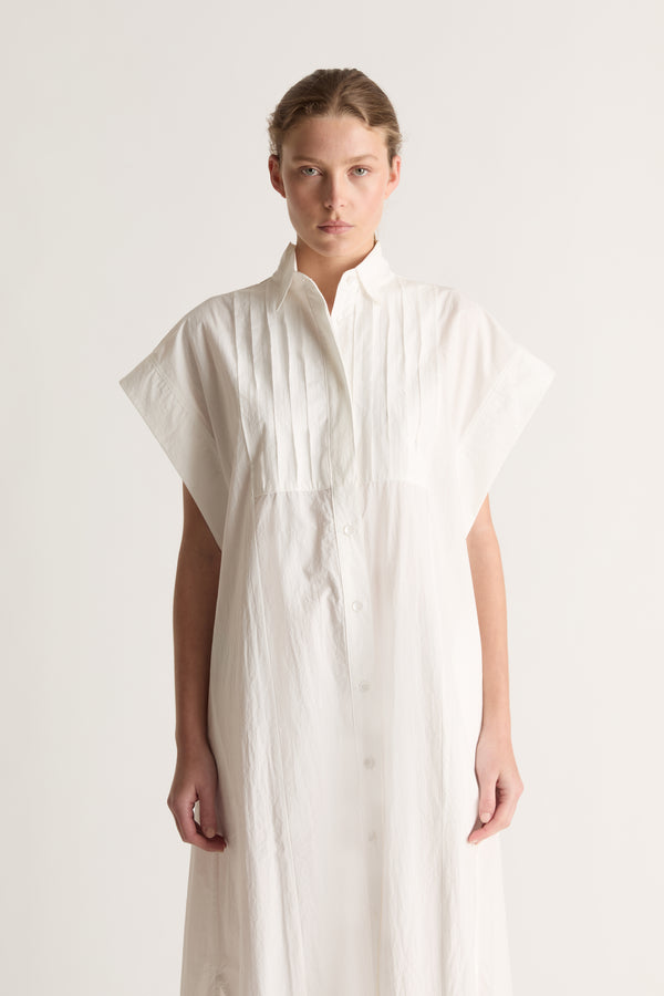 Close-up front view of a white shirt dress with a pointed collar, pin-tucked bib and wide cap sleeves.