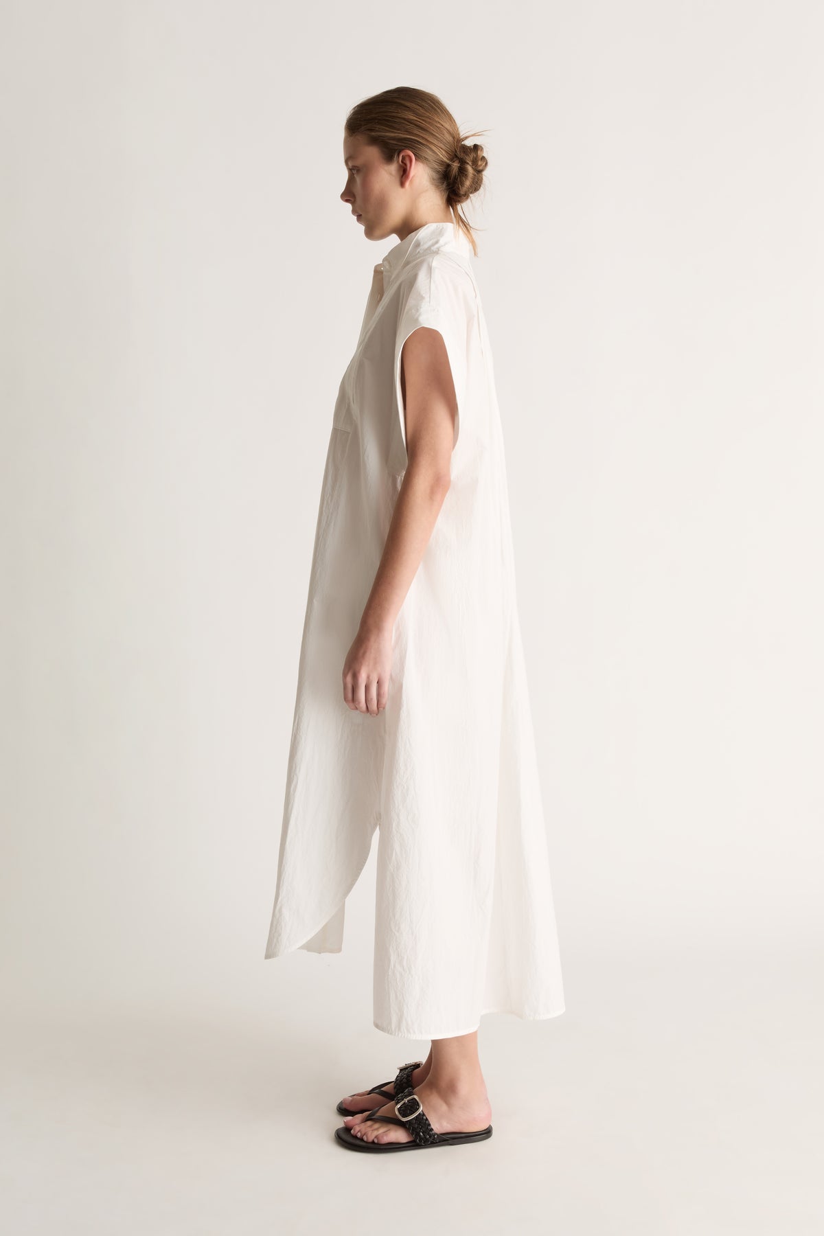 Side view of a white midi shirt dress with wide cap sleeves and a curved, split side hem.