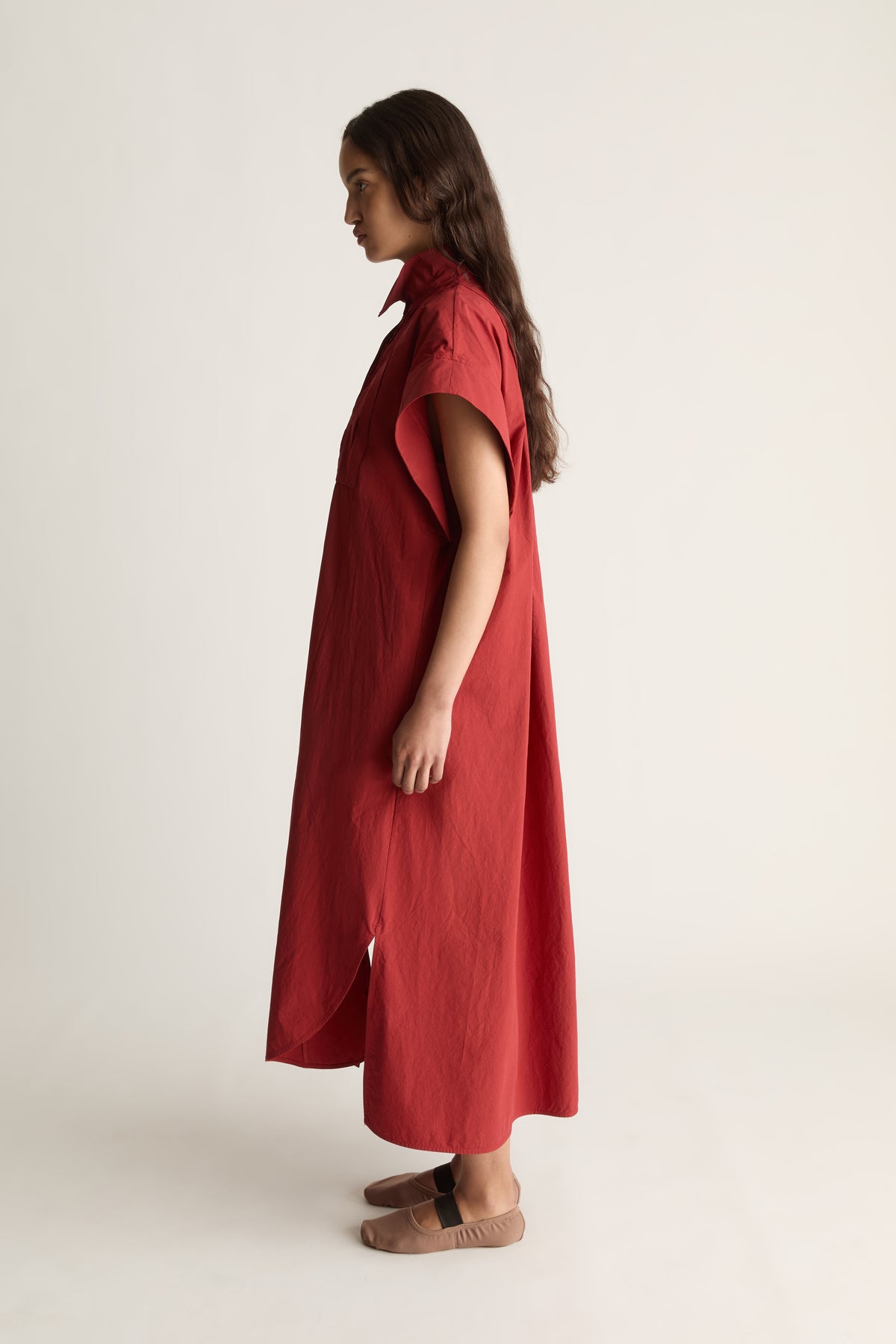 Side view of a woman in a red midi shirt dress with cap sleeve and curved hem