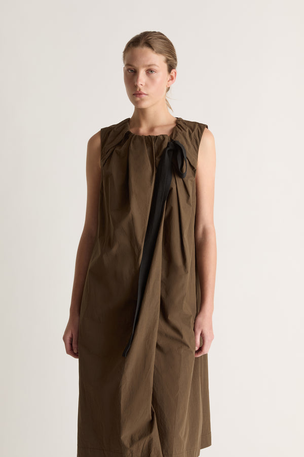 Close-up of a khaki dress with pleated round neckline and long black ribbon draped across the front