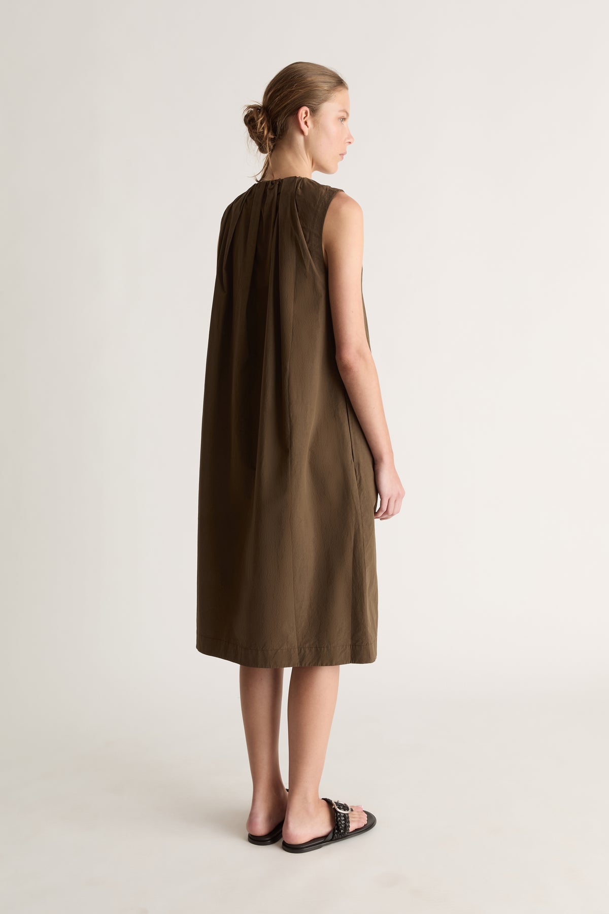 Back view of a woman with a bun in a khaki sleeveless midi dress with gathered back neckline