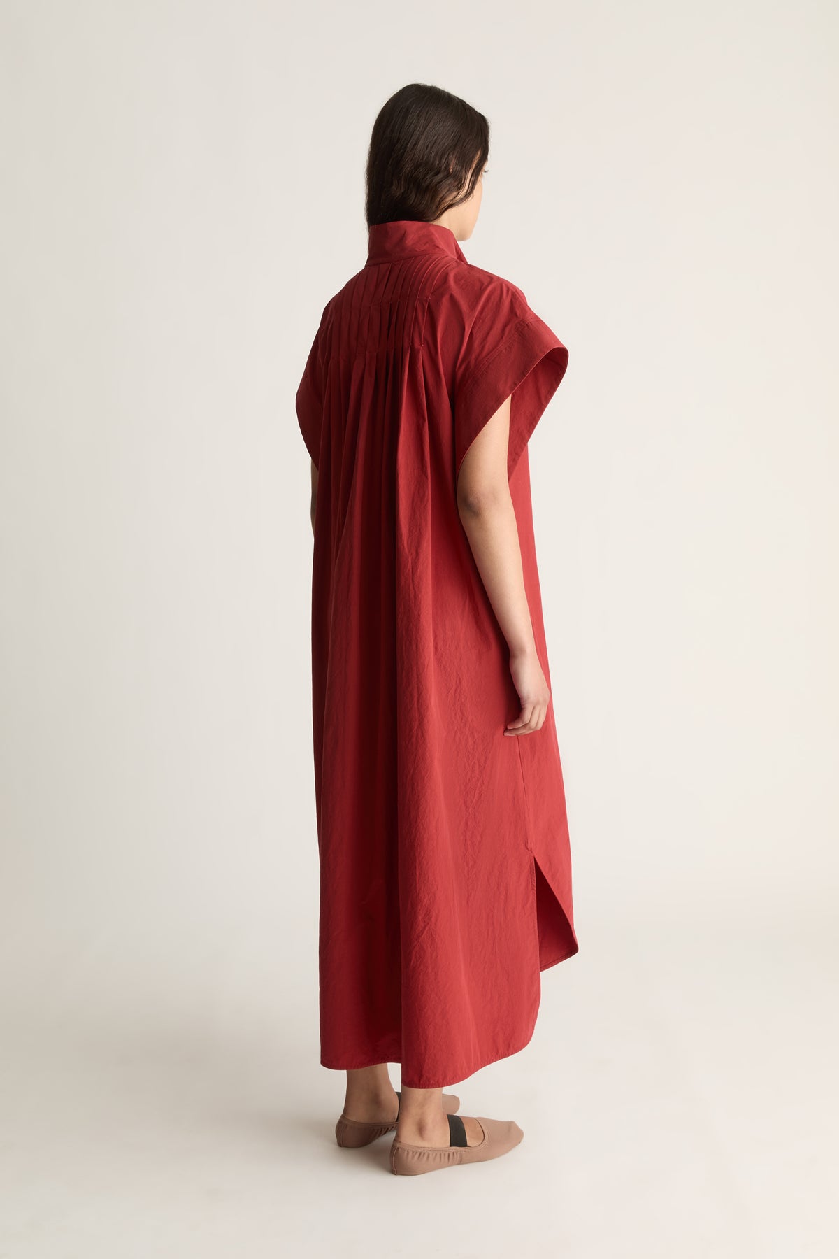 Back view of a woman in an oversized red shirt dress with back pleat and side slits