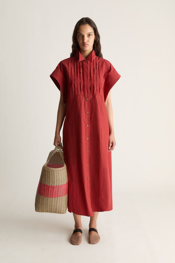 Front view of a woman in a red button-front shirt dress holding a woven basket with a pink stripe