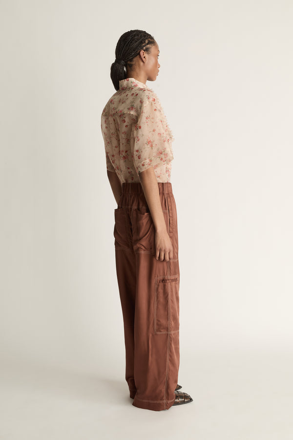 Person wearing a floral blouse and brown pants on a white background