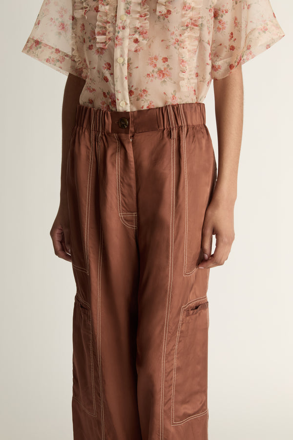 Person wearing a floral blouse and brown pants on a white background