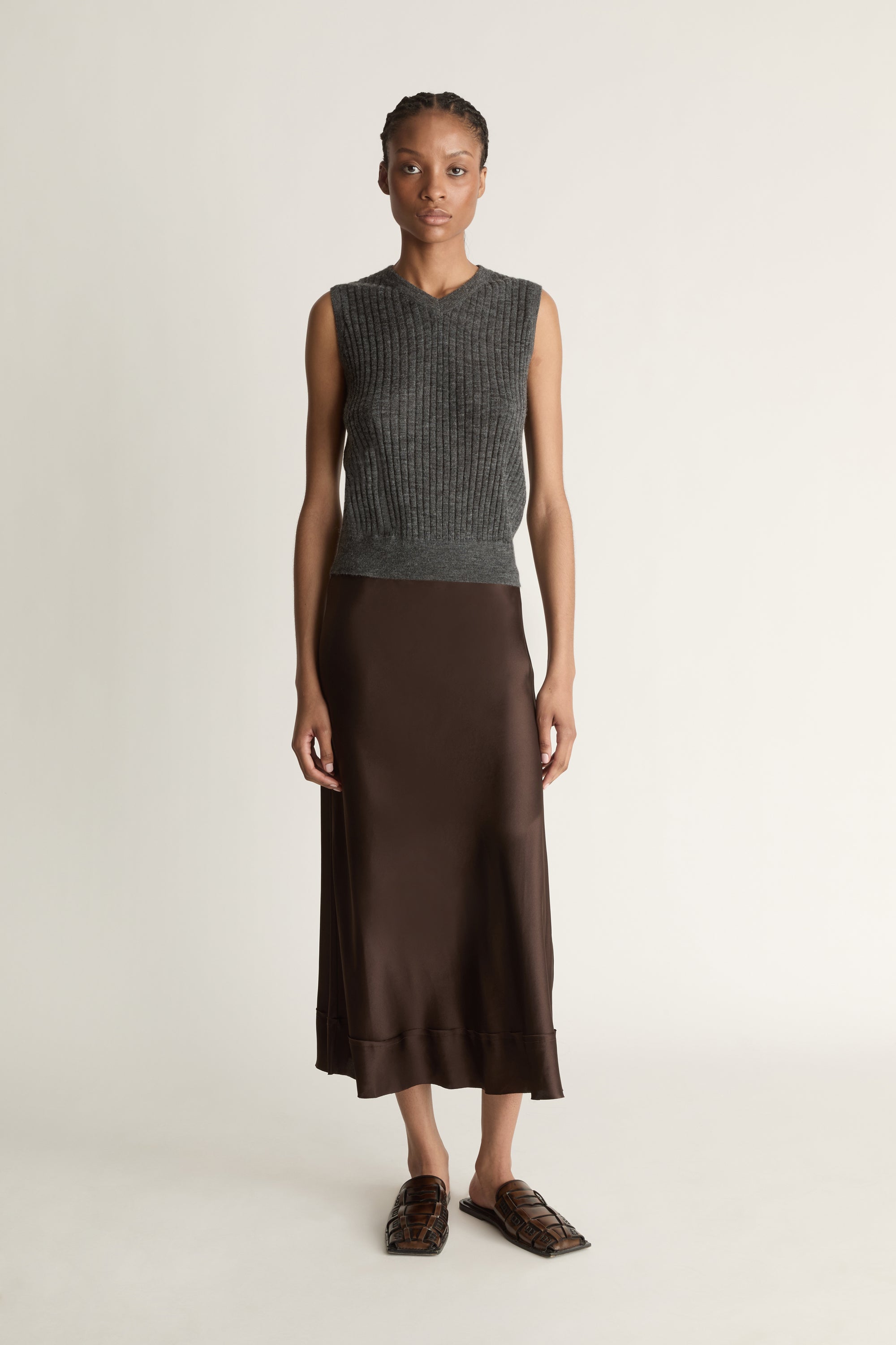 Woman wearing a sleeveless gray top and brown skirt on a plain background