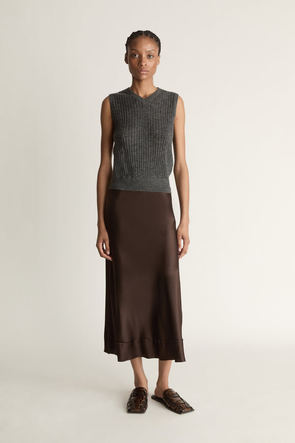 Woman wearing a sleeveless gray top and brown skirt on a plain background