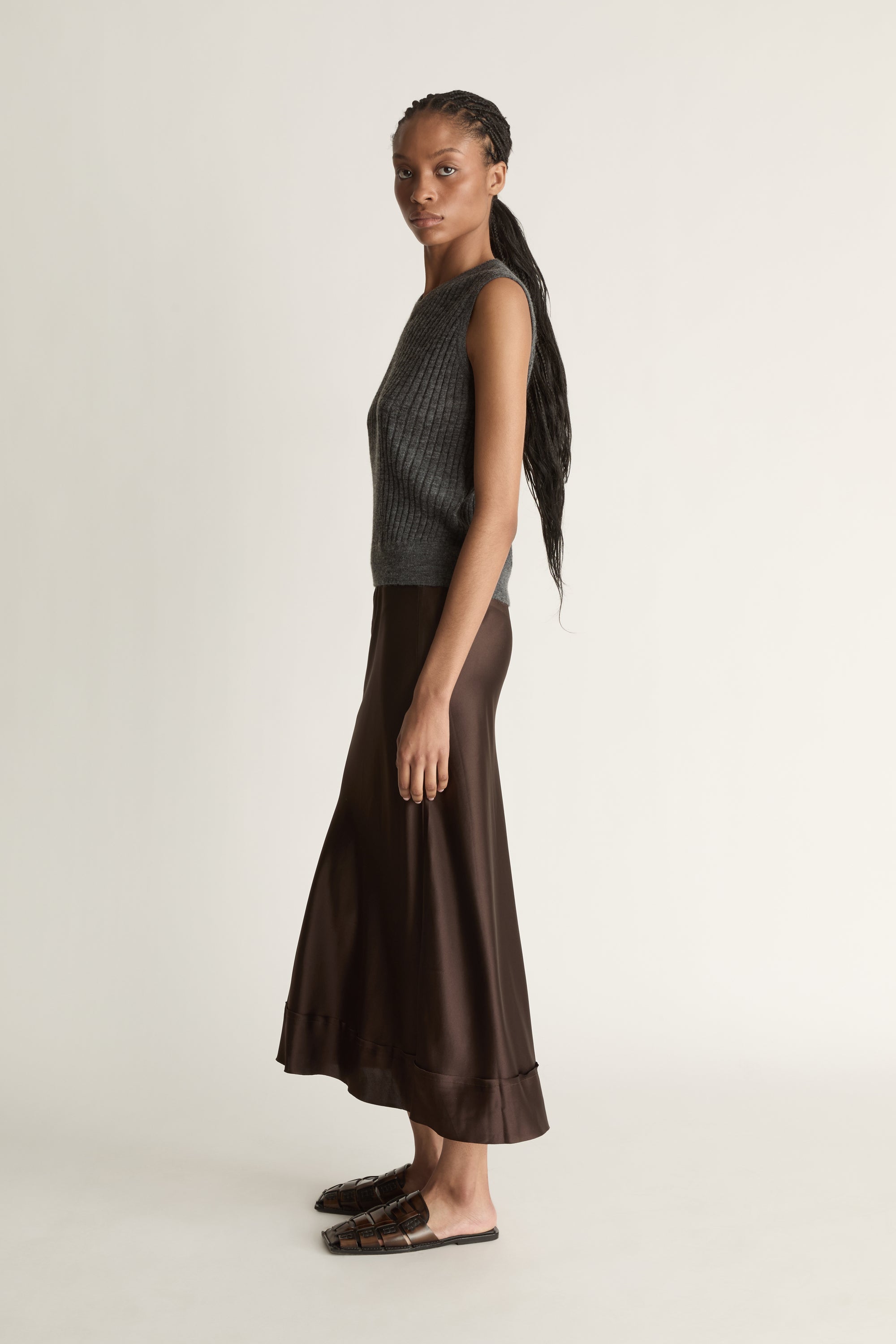 Woman wearing a sleeveless gray top and brown skirt on a plain background