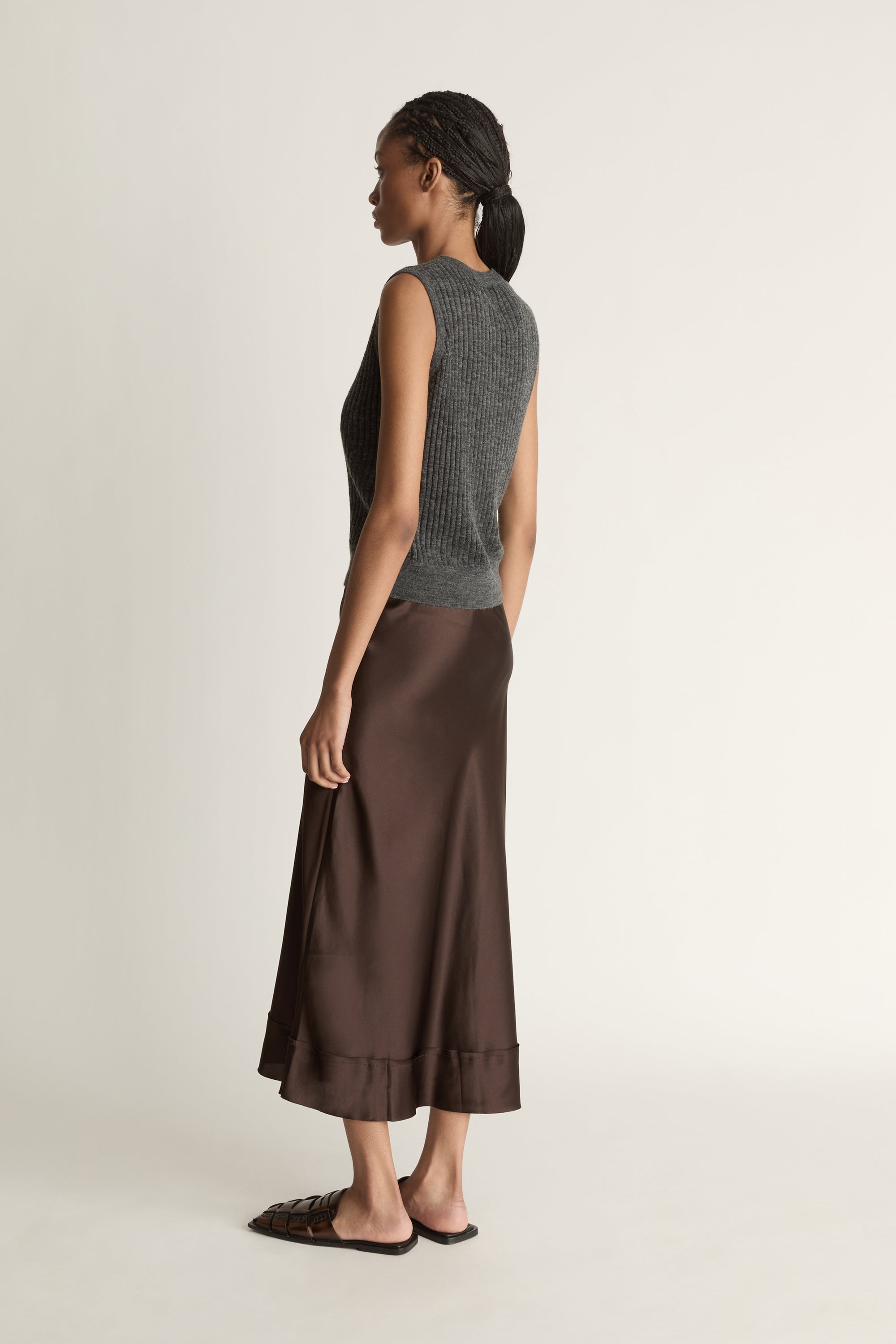 Woman wearing a sleeveless gray top and brown skirt on a plain background