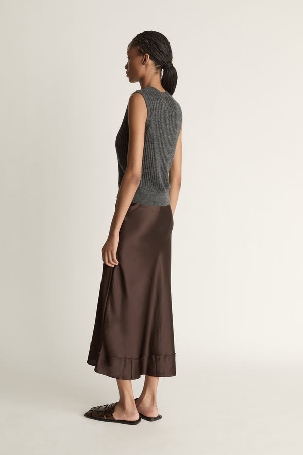 Woman wearing a sleeveless gray top and brown skirt on a plain background