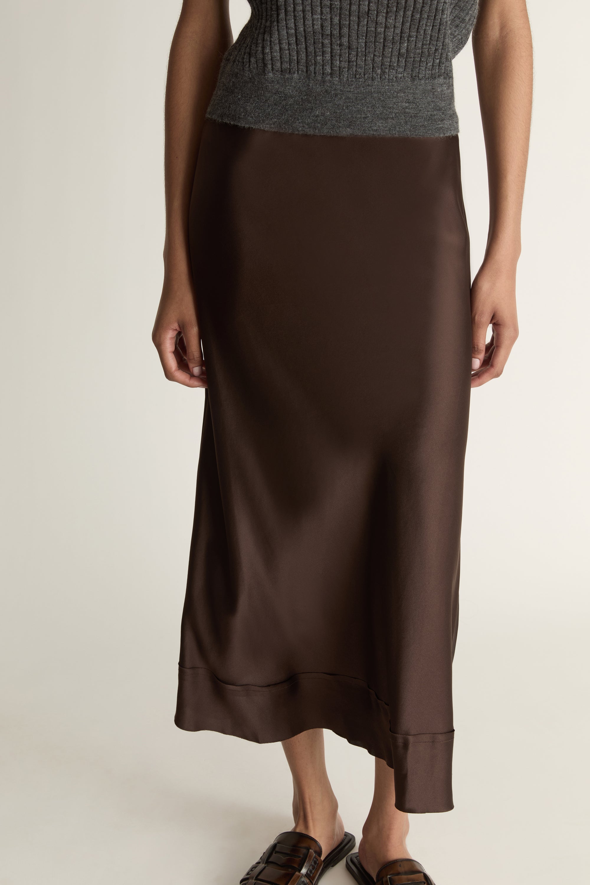 Woman wearing a sleeveless gray top and brown skirt on a plain background