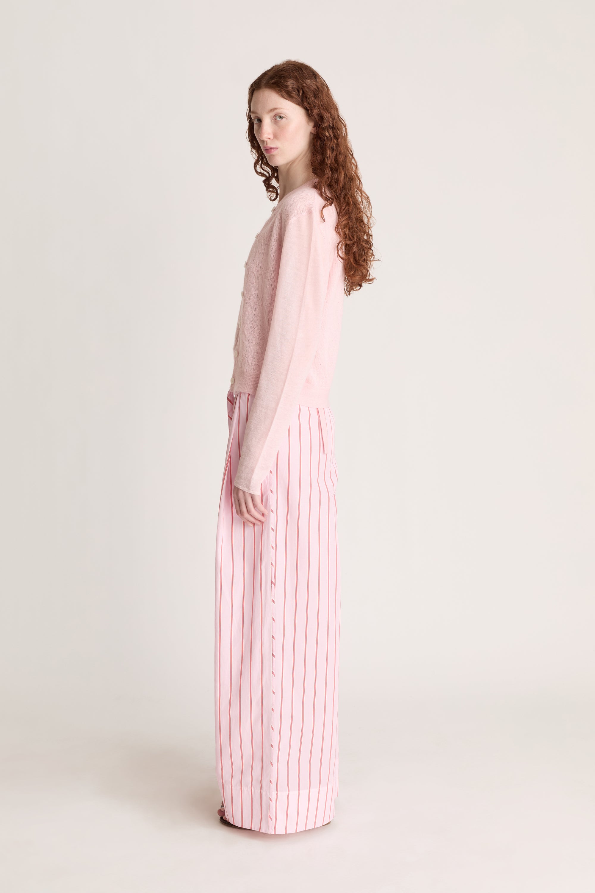 Woman wearing pink knit shirt and cardigan with pink striped pants on a white background