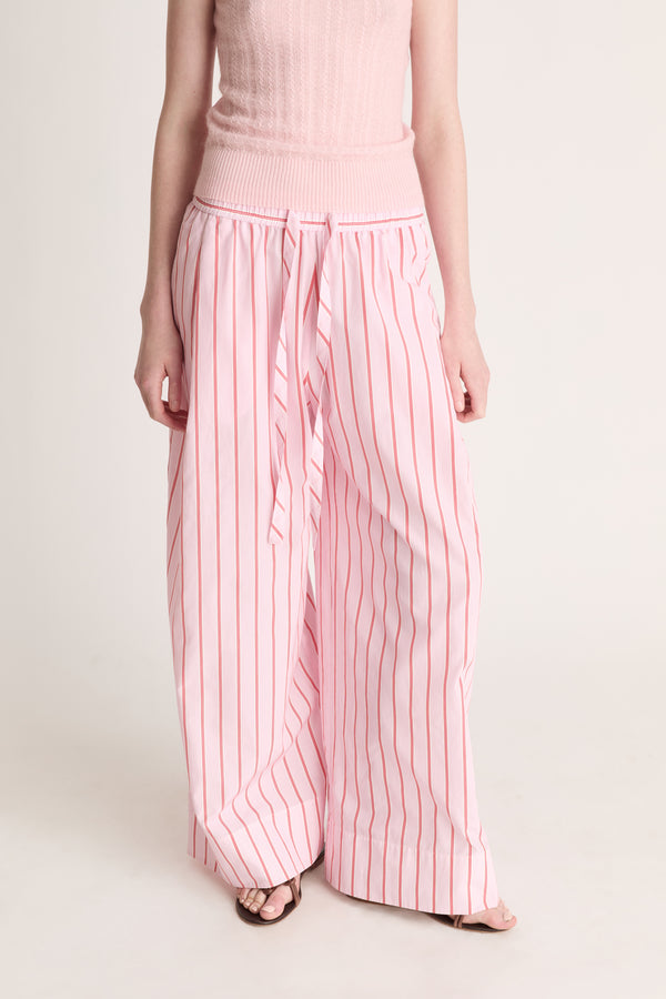 Close up of a woman wearing pink knit top with pink striped pants on a white background