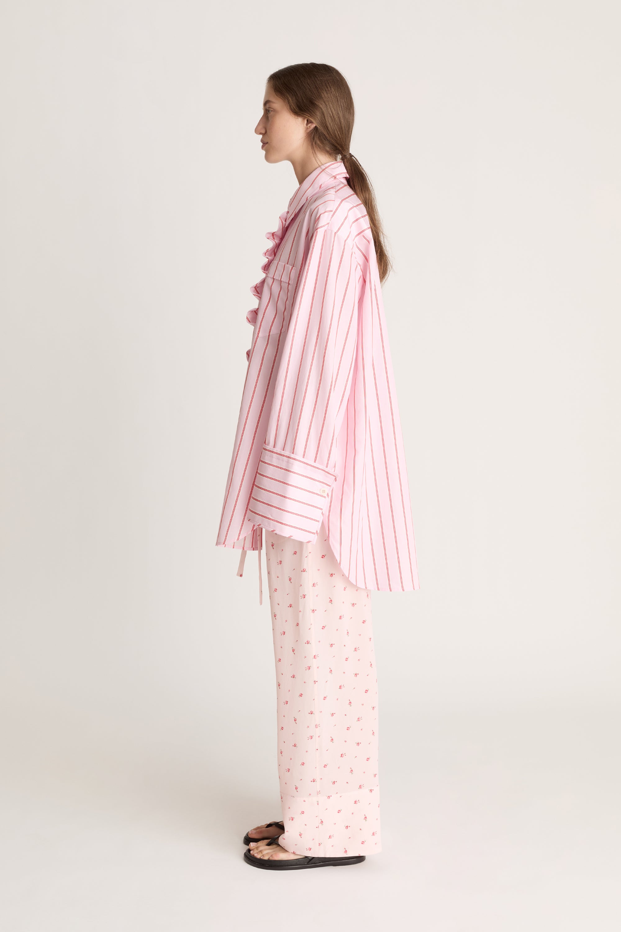 Woman wearing a pink striped shirt with floral pink pants on a white background