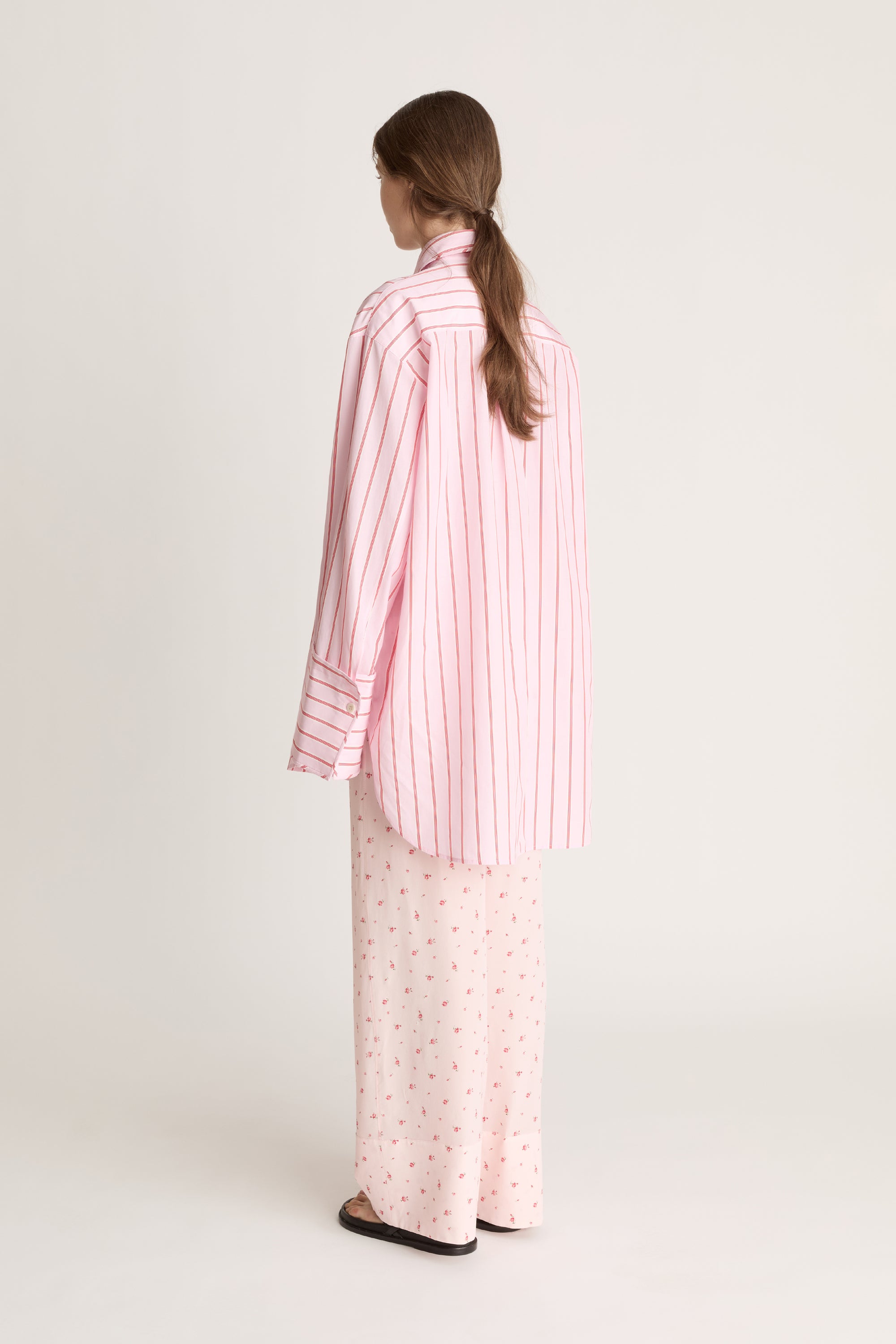 Woman wearing a pink striped shirt and pink floral pants on a white background