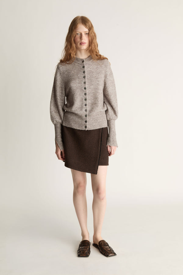 Woman wearing a gray sweater and brown skirt on a plain background