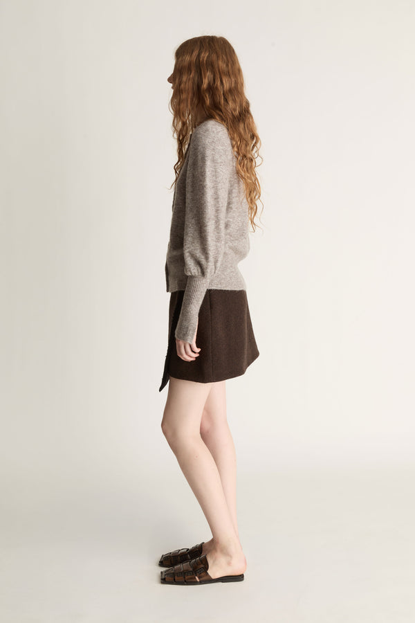 Woman wearing a gray sweater and brown skirt on a plain background