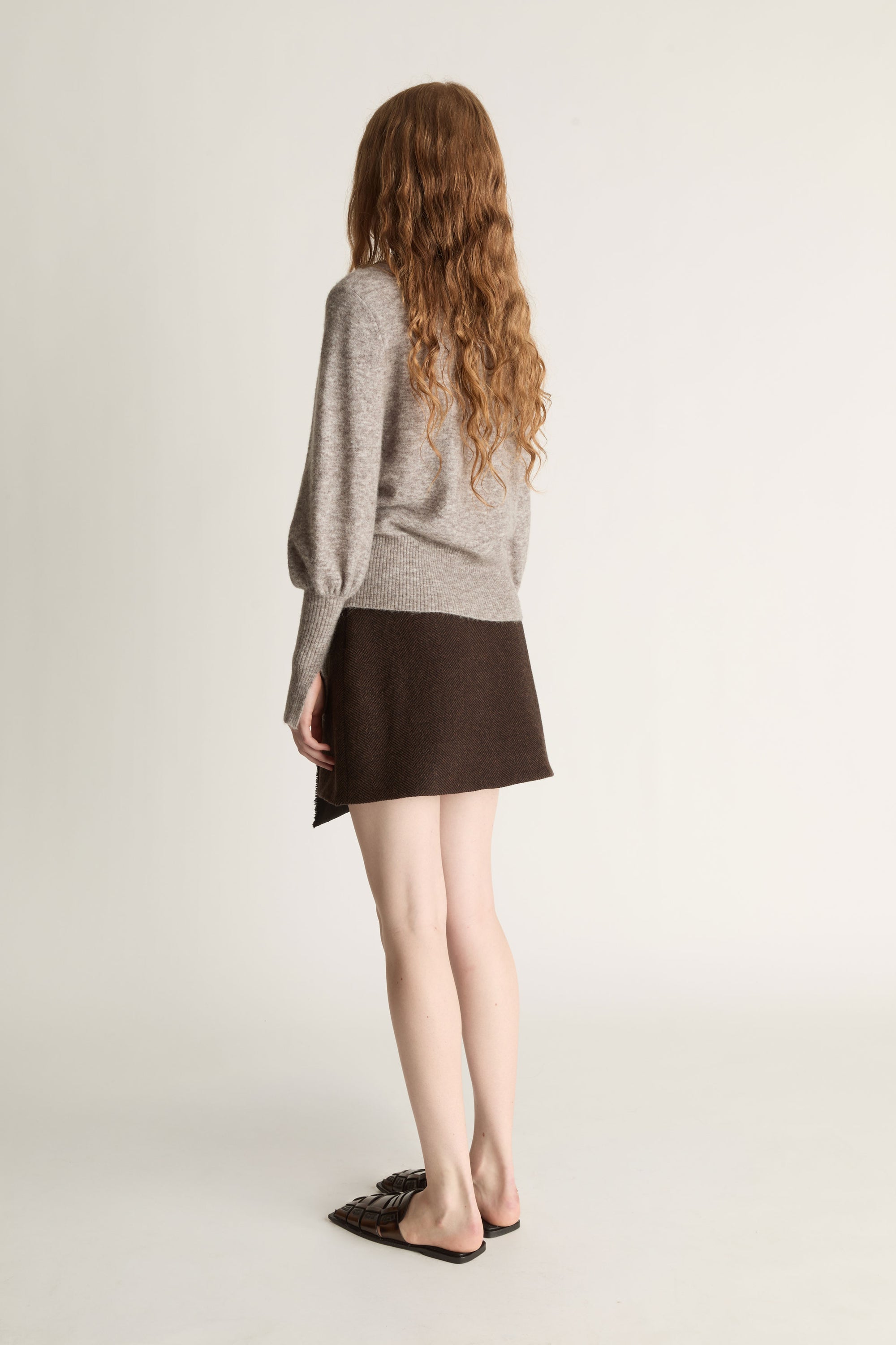 Woman wearing a gray sweater and brown skirt on a plain background