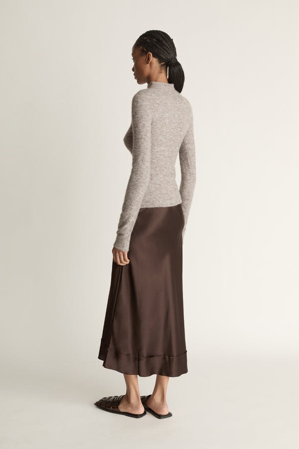 Woman wearing a gray turtleneck sweater and brown skirt against a beige background