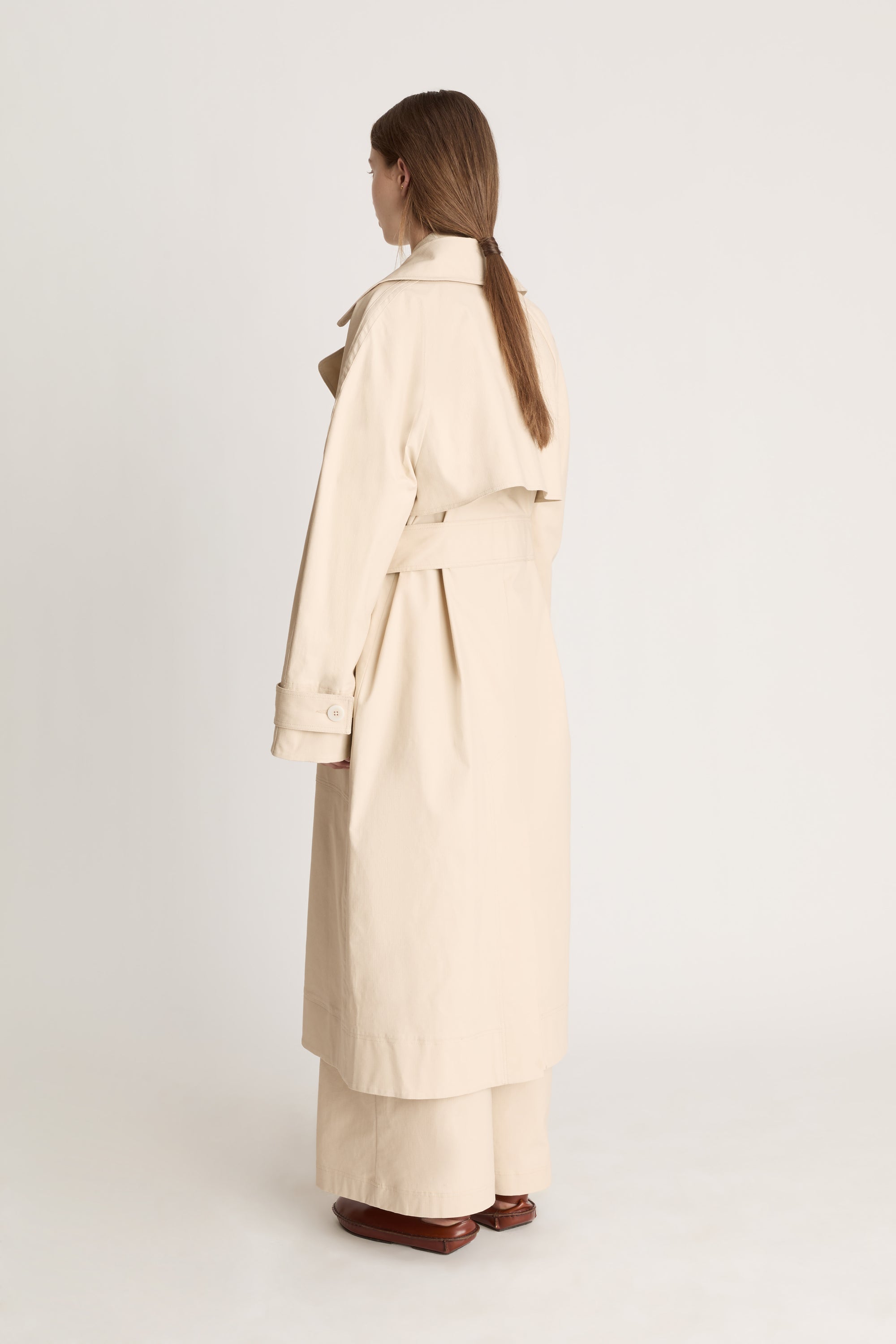 Woman wearing a beige trench coat holding a black bag on a white background