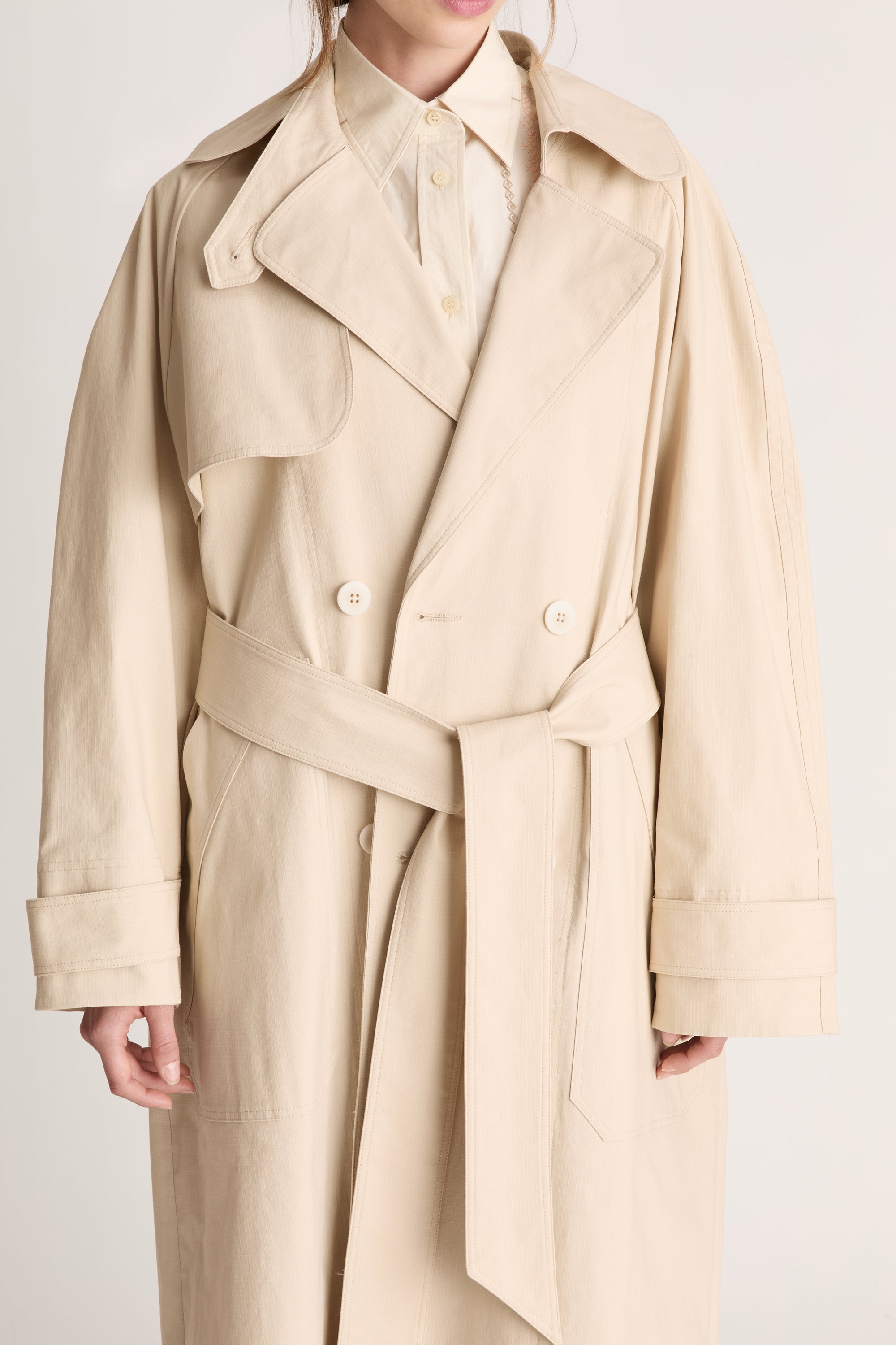 Beige trench coat worn by a person on a white background