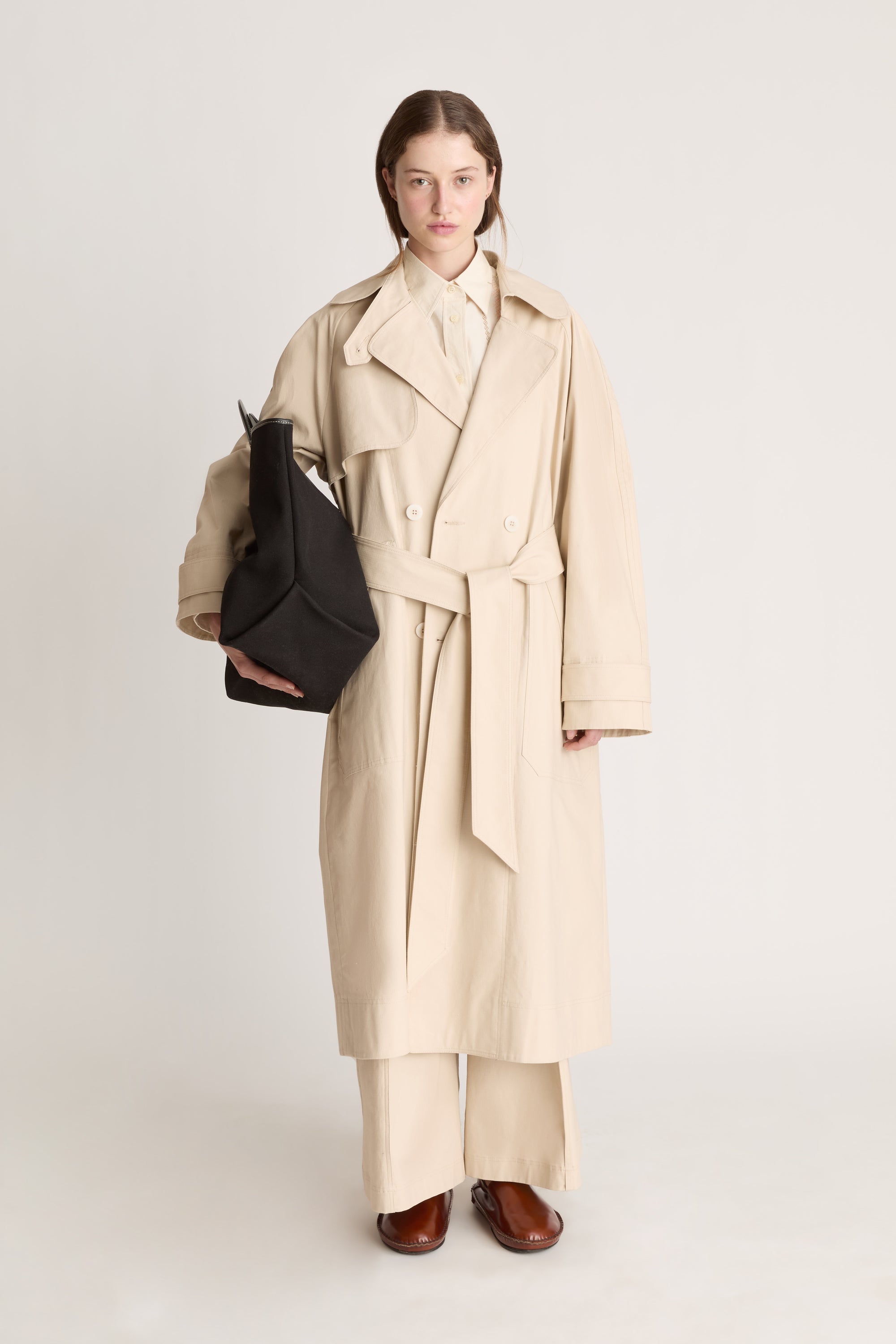 Woman wearing a beige trench coat holding a black bag on a white background